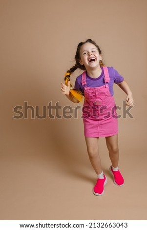 Exhilarated radiant happy female child having fun with two kanekalon pigtails of yellow color dressed in pink jumpsuit, purple t-shirt and pink sneakers on beige background. Stock photo © 