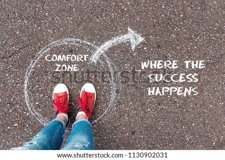 Exit from the comfort zone concept. Feet  in red sneakers standing inside circle comfort zone and outward arrow chalky on the asphalt.