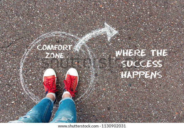 Exit from the comfort zone concept. Feet  in red\
sneakers standing inside circle comfort zone and outward arrow\
chalky on the asphalt.