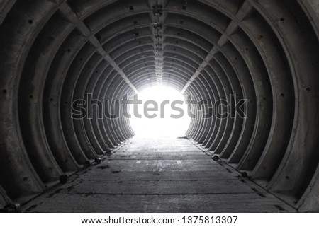 Exit from the empty white concrete tubing tunnel outside. Exit from bunker with light in the end. Inside empty concrete tubing tunnel. Abandoned tunnel with an apocalyptic feeling.