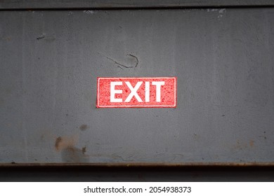 "Exit" red sticker sign which is sticked on grey rusty metal wall. Emergency sign object phot. Selective focus.