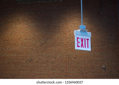 An Exit Sign With Stark Lighting And A Brick Wall Background.