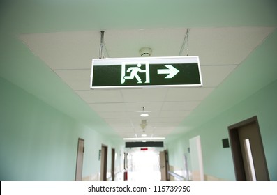 Exit Sign Suspended From The Ceiling Of Hospital Corridor.