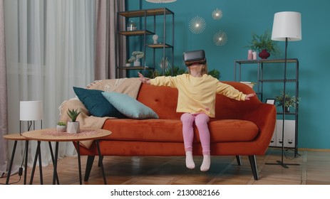 Exited Caucasian amazed toddler girl sitting on sofa in living room using headset helmet app to play simulation game. Watching virtual reality 3D 360 video. Teen school kid at home alone in VR goggles - Powered by Shutterstock