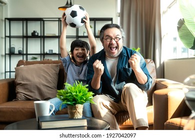 Exited Cheerful Joyful Asian Dad And Son Watching Sports On TV Cheering Favorite Soccer Team, Sitting Together On Sofa Couch At Home. Weekend With Father. Family Time, Online Tv Concept