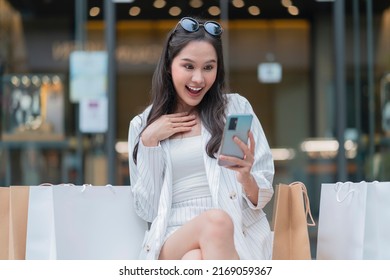 Exited joyful asia woman big surprise cloth discount sms show on smartphone ,asian woman using smartphone checking new promotion sale summer event at mall department store while relax on wooden bench