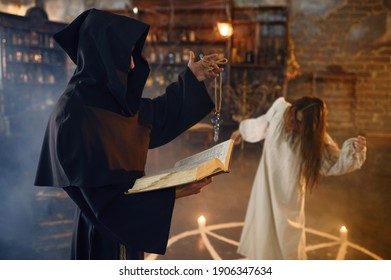 Exorcist in hood casting out demons from a woman - Shutterstock ID 1906347634