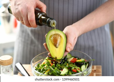 Exotic Avocado Seed Ingredient Poured Olive Oil. Male Hands Holding Half Tropical Fruit. Chef Cooking Healthy Vegetable Salad With Greens, Cucumber And Tomato. Dieting Culinary Food Horizontal Photo