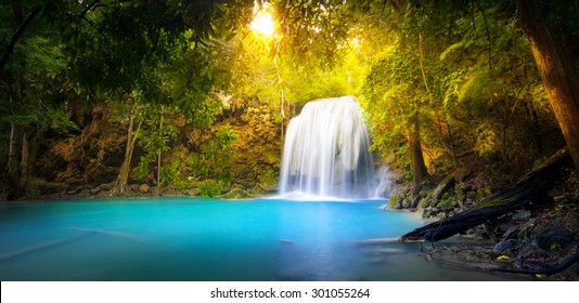 Exotic background of beautiful jungle forest with majestic waterfall falling into blue water lake and sun light rays shining through green leaves of tropical plants ant trees. Rainforest panorama - Powered by Shutterstock