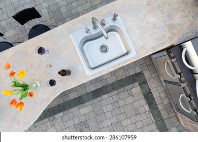 Exotic concrete counter top and sink in an outdoor kitchen set with two glasses and a bottle of red wine and a vase of tulips alongside a built in gas barbecue for healthy outdoor living