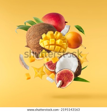 Exotic fruit mix, coconuts, mango, fig, passiflora, carambola falling in te air isolated on yellow background. Food levitation, zero gravity conception. High resolution image