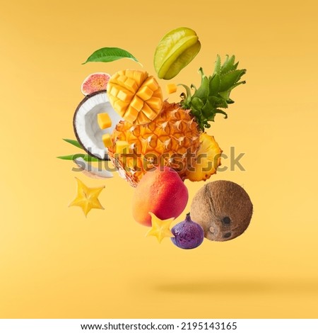 Exotic fruit mix, pineapple, coconuts, mango, fig, passiflora, carambola falling in te air isolated on yellow background. Food levitation, zero gravity conception. High resolution image