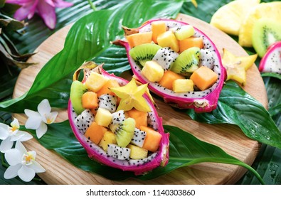 Exotic fruit salad served in half a dragon fruit on palm leaves with tropical flowers - Shutterstock ID 1140303860