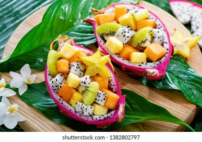 Exotic fruit salad served in half a dragon fruit on palm leaves with tropical flowers - Shutterstock ID 1382802797