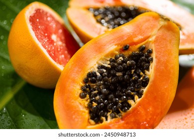 Exotic fruits background. Papaya and orange citrus fresh fruits on tropical leaf green background with shadows of palm tree. Halved fresh organic Papayas and grapefruit exotic fruits close up