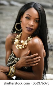 Exotic looking African American woman wearing black mini dress and jewellery with pearls posing sexy at outside location.