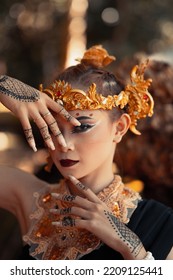 Exotic Woman In Her Bold Makeup While Wearing Golden Accessories On Her Head And Neck While In A Black Dress Inside The Forest