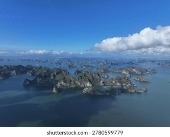 An expansive aerial view captures dramatic karst islands emerging from calm turquoise waters beneath a vast clear blue sky with scattered white clouds.
