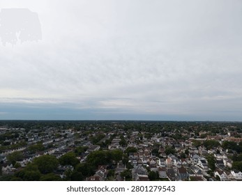 Expansive aerial view capturing the dense residential landscape of hollis, queens, new york city, featuring numerous houses, lush trees, and urban sprawl under a cloudy sky