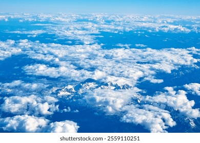 Expansive aerial view showcasing snow-covered mountain peaks beneath a dense formation of fluffy clouds. the clear blue sky accentuates the majestic landscape, offering a serene and tranquil atmospher - Powered by Shutterstock