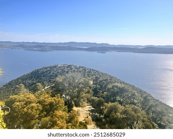 Expansive coastal vista with rolling hills, lush greenery, and calm blue waters under a clear sky. Ideal for themes of nature, serenity, and panoramic landscapes. - Powered by Shutterstock