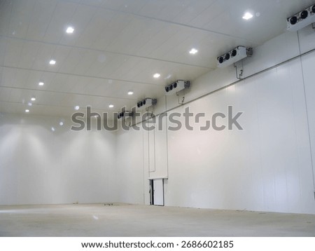 An expansive, empty cold storage room featuring insulated white walls, ceiling lights, and industrial cooling units mounted on the walls.
