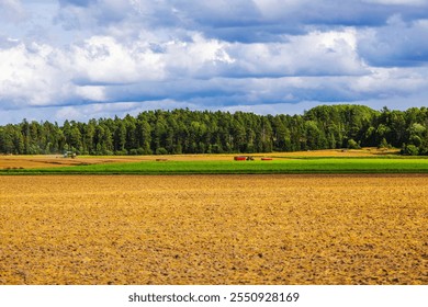 Expansive farmland with plowed fields, green pastures, and tractor working under cloudy sky near forest edge. Sweden. - Powered by Shutterstock