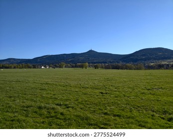 Expansive grassy plain with distant spired summit, uninterrupted foreground, crisp blue sky, subtle village