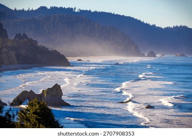 An expansive, high-angle aerial view capturing the wide, sandy beach along Tillamook Bay, with the Pacific Ocean and surrounding coastal landscape under a clear, bright, sunny sky in Oregon