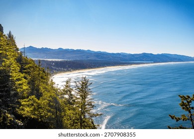 An expansive, high-angle aerial view capturing the wide, sandy beach along Tillamook Bay, with the Pacific Ocean and surrounding coastal landscape under a clear, bright, sunny sky in Oregon