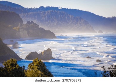 An expansive, high-angle aerial view capturing the wide, sandy beach along Tillamook Bay, with the Pacific Ocean and surrounding coastal landscape under a clear, bright, sunny sky in Oregon