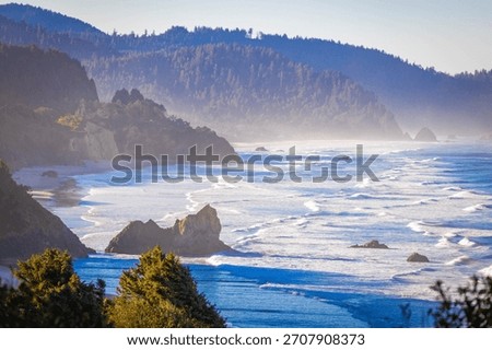An expansive, high-angle aerial view capturing the wide, sandy beach along Tillamook Bay, with the Pacific Ocean and surrounding coastal landscape under a clear, bright, sunny sky in Oregon