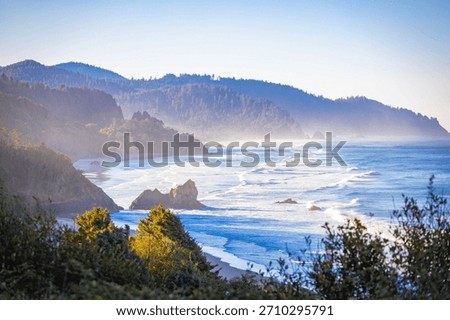 An expansive, high-angle aerial view capturing the wide, sandy beach along Tillamook Bay, with the Pacific Ocean and surrounding coastal landscape under a clear, bright, sunny sky in Oregon