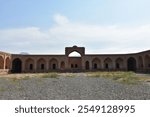 An expansive historical caravanserai with a majestic central courtyard, showcasing traditional brickwork and symmetrical arches. Once a bustling stop for travelers, now a serene remnant of cultural he