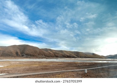 Expansive mountain landscape under a dramatic cloudy sky. A river flows across the valley with a road cutting through the scene, ideal for travel, adventure, freedom, solitude, and nature concepts
