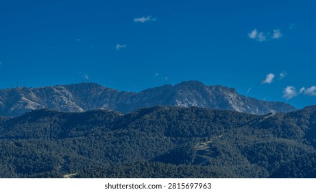 Expansive mountain range featuring vast forest slopes and rocky peaks under a bright blue sky