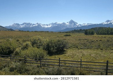 Expansive mountain range rises beyond open ranchland and fencing in southwestern Colorado.