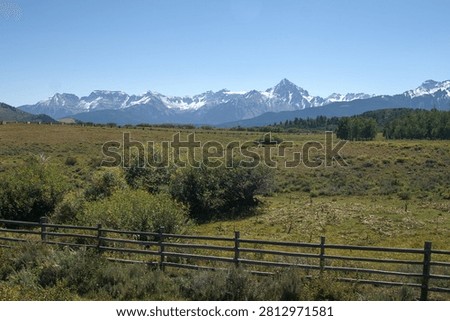 Expansive mountain range rises beyond open ranchland and fencing in southwestern Colorado.