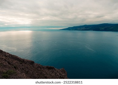 Expansive ocean view from a rugged cliffside, with calm waters and a dramatic cloudy sky, perfect for travel or nature-related projects. - Powered by Shutterstock