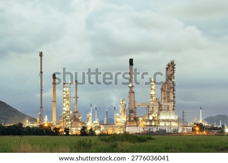 An expansive oil refinery complex set against a dramatic twilight sky in Bang Lamung District, Chonburi Province, Thailand. This industrial landscape features a network of towering distillation columns, steel frameworks, and intricate pipelines designed for large-scale petroleum refining and petrochemical manufacturing. Soft evening light blends with the glow of facility illumination, creating a striking contrast between advanced engineering and the fading horizon.

The scene highlights modern energy infrastructure in Southeast Asia, showcasing high-capacity processing units, storage tanks, and interconnected systems essential for fuel production, chemical processing, and energy supply. Metallic structures rise prominently, reflecting both efficiency and technological progress, while vapor trails and subtle emissions add realism to the working environment.

Located within Thailand’s Eastern Economic Corridor, this refinery represents a vital component of regional industry and global markets. The composition captures both the complexity and scale of heavy industry, making it ideal for themes such as industrial development, energy production, oil and gas operations, refinery engineering, and petrochemical technology.

The twilight backdrop enhances visual appeal, with deep blue and warm orange tones merging above the facility, emphasizing a balance between nature and industrial advancement. This setting is perfect for illustrating concepts like power generation, fossil fuel processing, infrastructure investment, and modern manufacturing.

Overall, the image conveys a powerful impression of industrial capability, economic growth, and technological sophistication, making it suitable for use in energy sector presentations, business reports, environmental discussions, and commercial design projects focused on oil refining, petrochemical plants, and global industry.