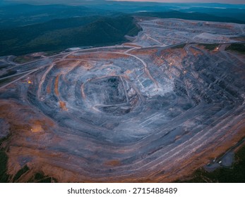Expansive open pit mining operation in hilly terrain at dusk by drone.