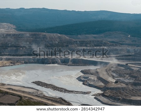 Expansive open pit mining site with terraced quarry, heavy trucks and dust plumes framed by forested hills in British Columbia, Canada.