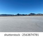 Expansive salt flats under a clear blue sky, with distant mountain ranges creating a stunning natural horizon