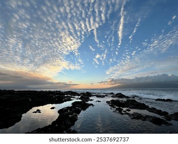 Expansive sunset sky with dramatic cloud patterns over a rocky shoreline and tide pools reflecting the colorful evening light - Powered by Shutterstock