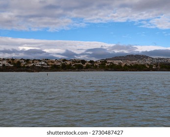 Expansive water under dramatic clouds framing jagged ridge and compact coastal village on the horizon.