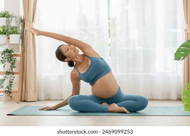 An expectant Asian woman demonstrates a graceful side stretch pose while practicing prenatal yoga in a well-lit promotes flexibility and well-being, essential for a healthy pregnancy - Powered by Shutterstock