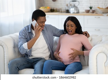 Expectant Black Woman Having Prenatal Contractions, Her Boyfriend Reaching Doctor On Smartphone From Home. African American Lady Giving Birth To Baby, Her Husband Calling For Medical Assistance