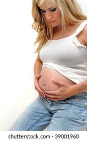 Expectant female gently holds her growing stomach to transfer her love to her unborn child.  She is wearing jeans and a white shirt.