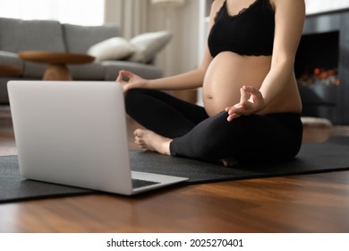 Expectant mom practicing meditation, watching online video lesson. Pregnant woman siting, in lotus pose at laptop, keeping zen fingers, relaxing, doing yoga. Fitness in pregnancy. Close up