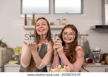 Expectant mother and daughter decorating cupcakes on a kitchen table, having a good time together while eating freshly baked pastries